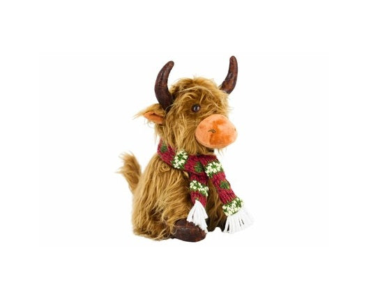 A plush Highland cow toy with shaggy brown fur, dark brown horns, and an orange snout, wearing a red knit scarf with green and white floral patterns and white tassels, isolated on a white background.