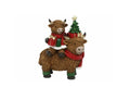 A festive Christmas figurine featuring two shaggy Highland cows, one carrying the other on its back. The cow wears a red scarf and green leg wraps, while the passenger wears a red and green outfit and holds a small decorated Christmas tree with a gold star topper.