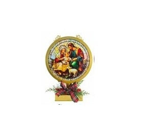 A circular Christmas nativity wall hanging with a gold-toned frame, featuring an illustration of Mary, Joseph, baby Jesus, and a sheep, mounted on a small decorative base with red ribbon and greenery.